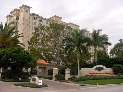 A large beige multi-story senior living facility with palm trees and a gated entrance.