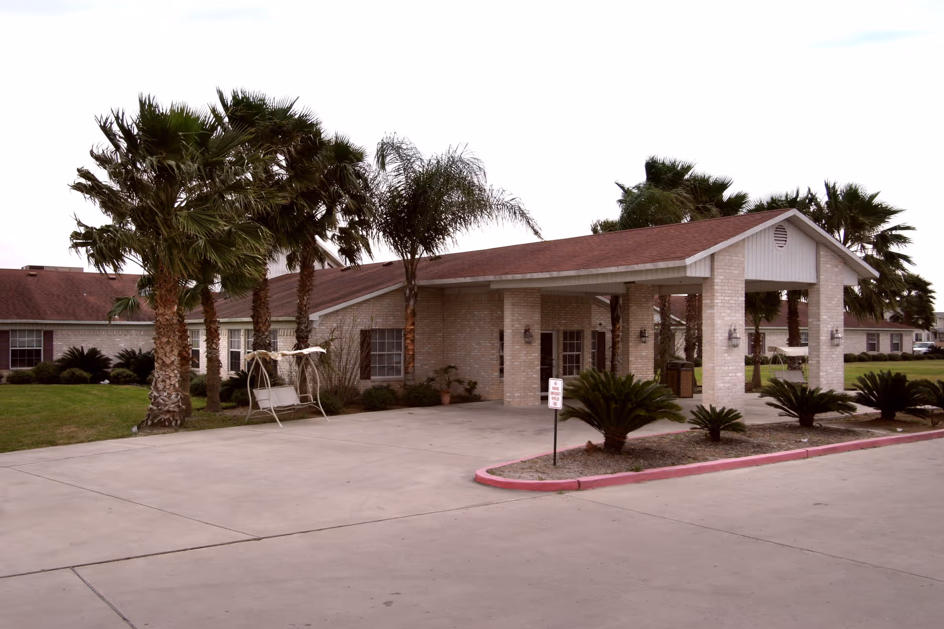 Front entrance of a single-story nursing facility with a covered porte-cochere, palm trees, and a driveway.