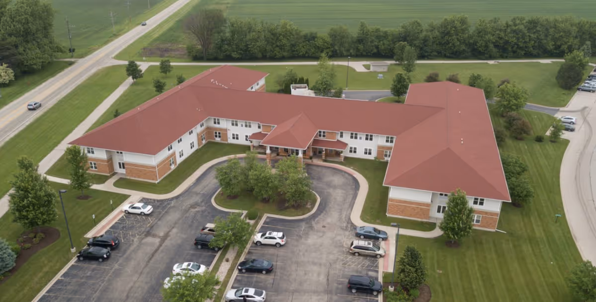 Aerial view of Heritage Woods of DeKalb, a red-roofed senior living center with parking.