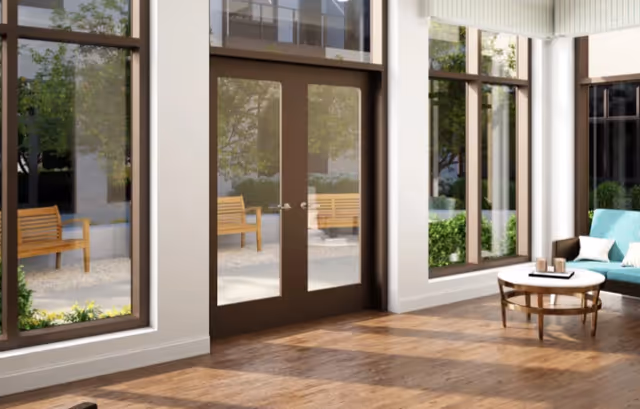 Bright lounge with floor-to-ceiling windows and double glass doors opening to an outdoor bench area, a teal sofa and round coffee table on a wooden floor.