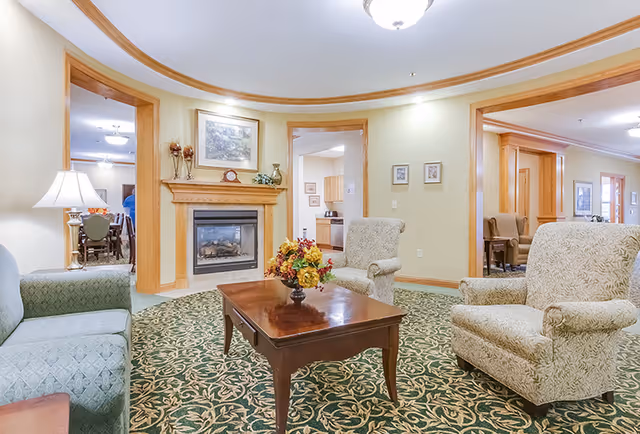 Common living room area with upholstered chairs, a wooden coffee table topped with a floral arrangement, and a fireplace under a curved ceiling detail.