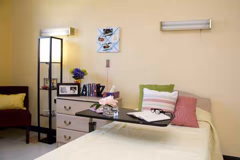 A senior facility bedroom with a bed, dresser, and overbed table.