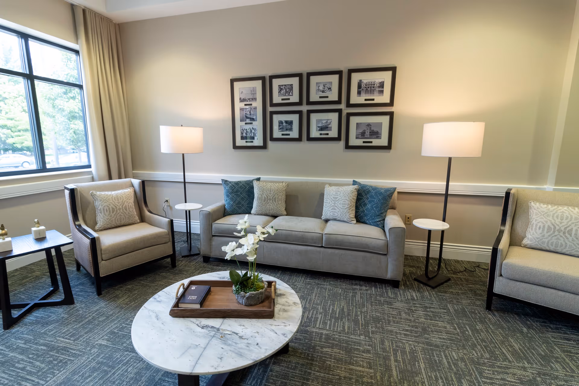 Bright seating area with a sofa, two armchairs, floor lamps, marble coffee table and framed photos on the wall.