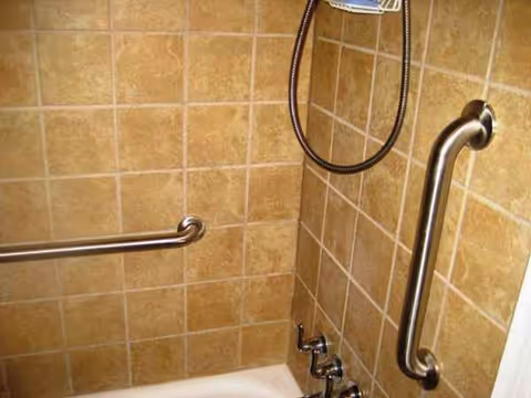 Tile bathroom with grab bars and a handheld shower head in a senior living facility.
