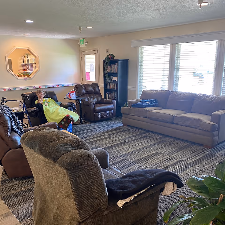 Cozy lounge area in a senior living facility with multiple chairs and a resident resting.
