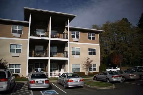 Three-story Olympic Place by Bonaventure exterior with balconies, parking, and surrounding trees.
