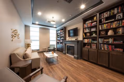 Cozy lounge with built-in bookshelves and fireplace, wall-mounted TV, seating, coffee table, and large window.