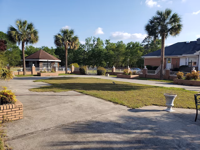 Well-maintained courtyard with palm trees, a gazebo, brick planters and surrounding single-story buildings under a blue sky.