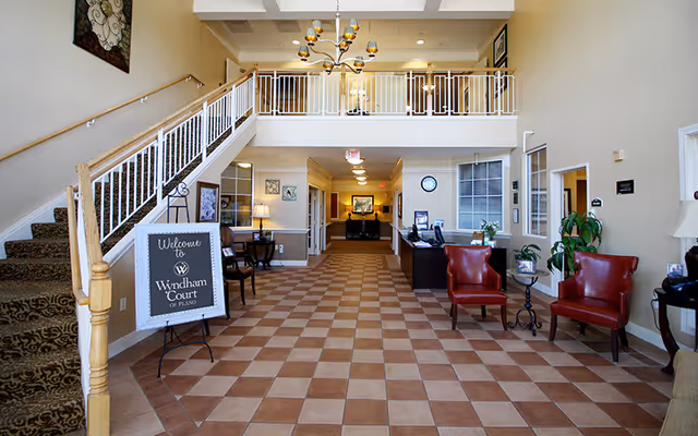 Main lobby of Wyndham Court of Plano with a reception desk, seating, staircase, and a welcome sign.