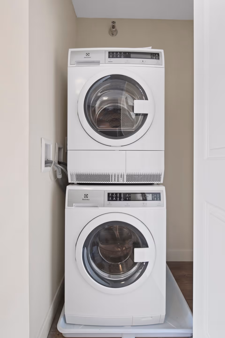 Stacked white front-loading washer and dryer units in a small laundry nook with beige walls and a white door partially visible on the right.