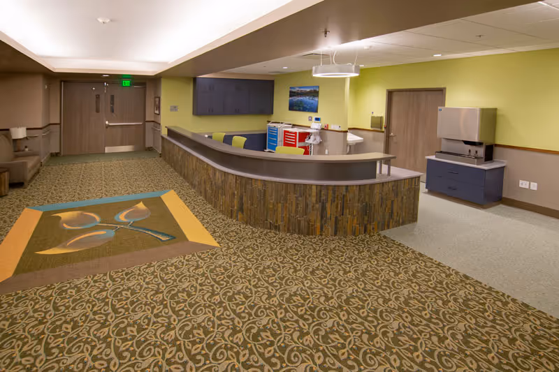 Interior reception area with a curved nurse's station, patterned carpet, seating, and green-accented walls.