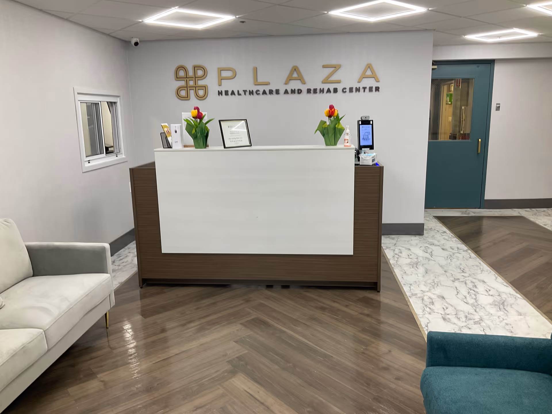 Reception desk and waiting area with sofas, tulip arrangements, and a 'Plaza Healthcare and Rehab Center' sign on the wall.