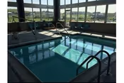 Indoor swimming pool with handrails and large windows overlooking a grassy landscape.