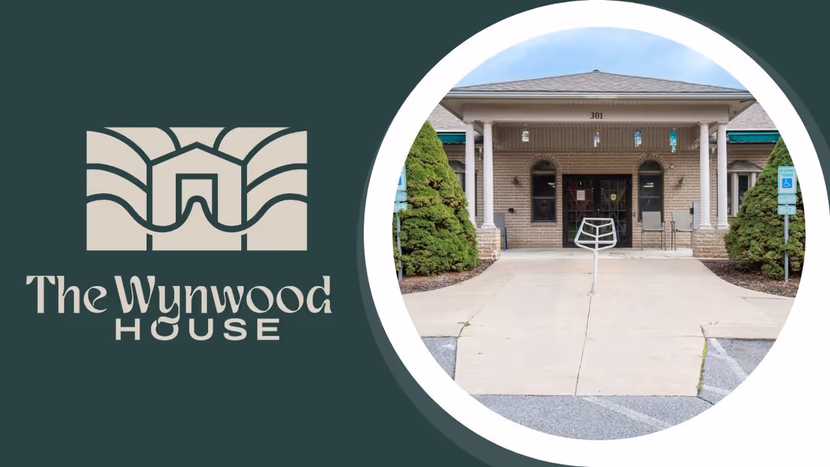 Front exterior view of The Wynwood House building entrance with a covered porch, two large bushes on either side, and a concrete walkway leading to the door.