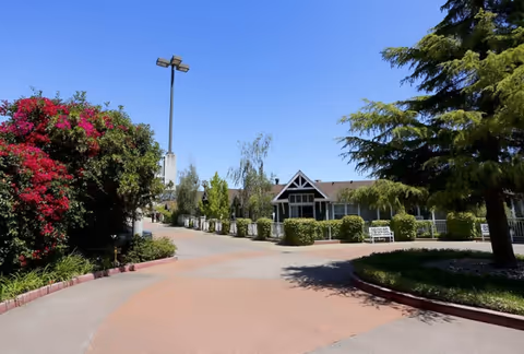 Curved brick-paved walkway leads to a single-story senior living facility with landscaping.