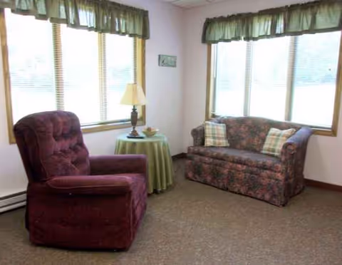 Cozy living room with burgundy recliner, floral sofa, and lamp by large windows.