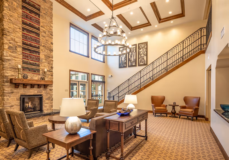Luxurious senior living lounge with stone fireplace, chandelier, and staircase.