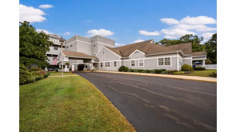 Front exterior of a nursing and rehabilitation center with a driveway, entrance canopy, and landscaped lawn under a blue sky.