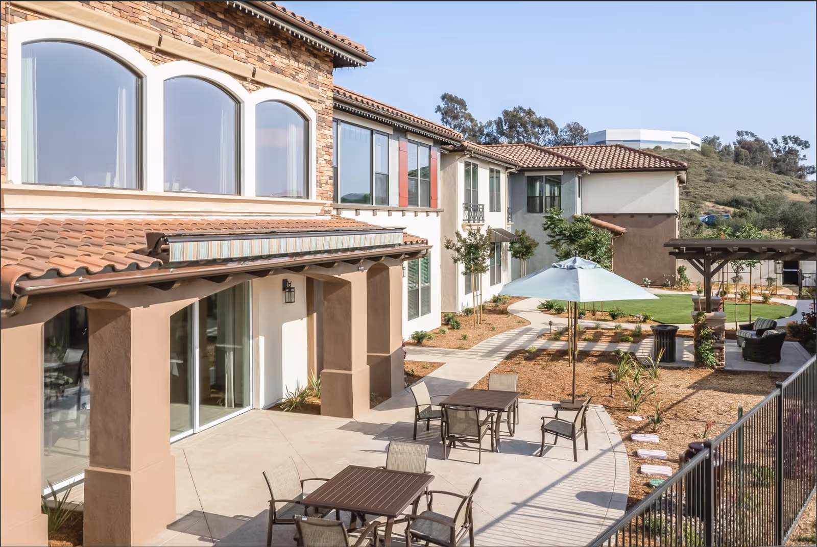 Exterior courtyard with patio tables, chairs, umbrella and a two-story building facade.