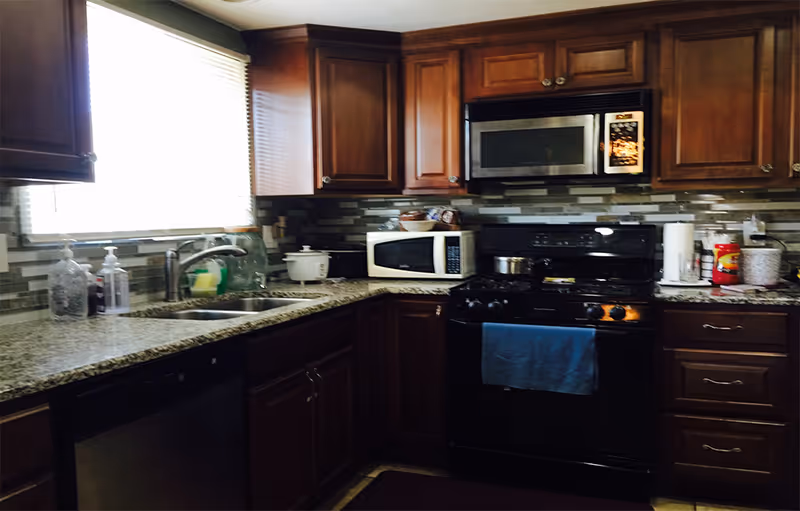 Kitchen with dark wood cabinets, granite countertops, a sink under a window, microwave, and a black stove.