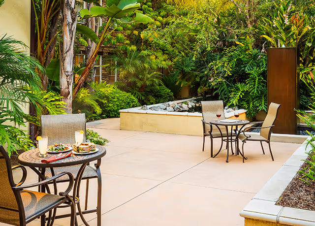 Outdoor courtyard patio with bistro tables and chairs, lush tropical landscaping, and a small water feature.