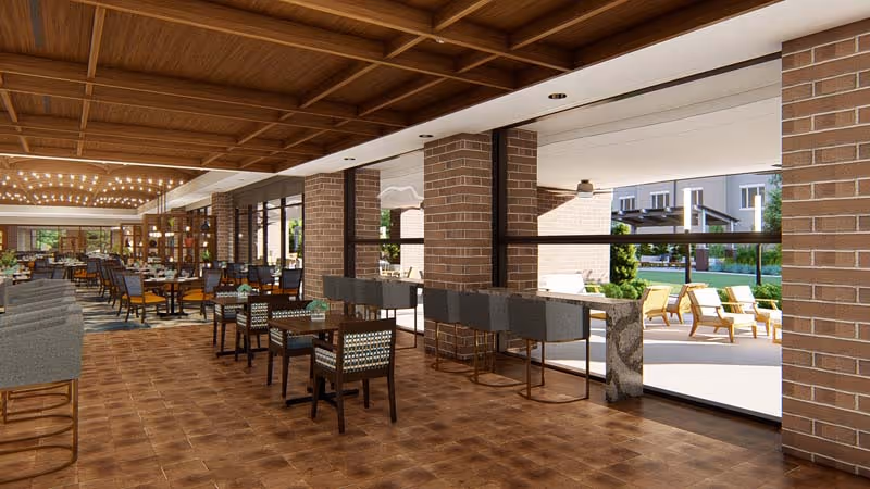 Spacious dining area with wooden tables and chairs arranged neatly, featuring a tiled floor and brick pillars. Large windows provide a view of an outdoor patio with lounge chairs and greenery. The ceiling has a wooden grid design with recessed lighting.