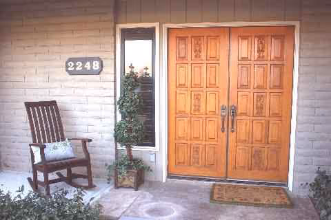 Front entrance of a senior living facility with wooden double doors, a bench, and potted plants.