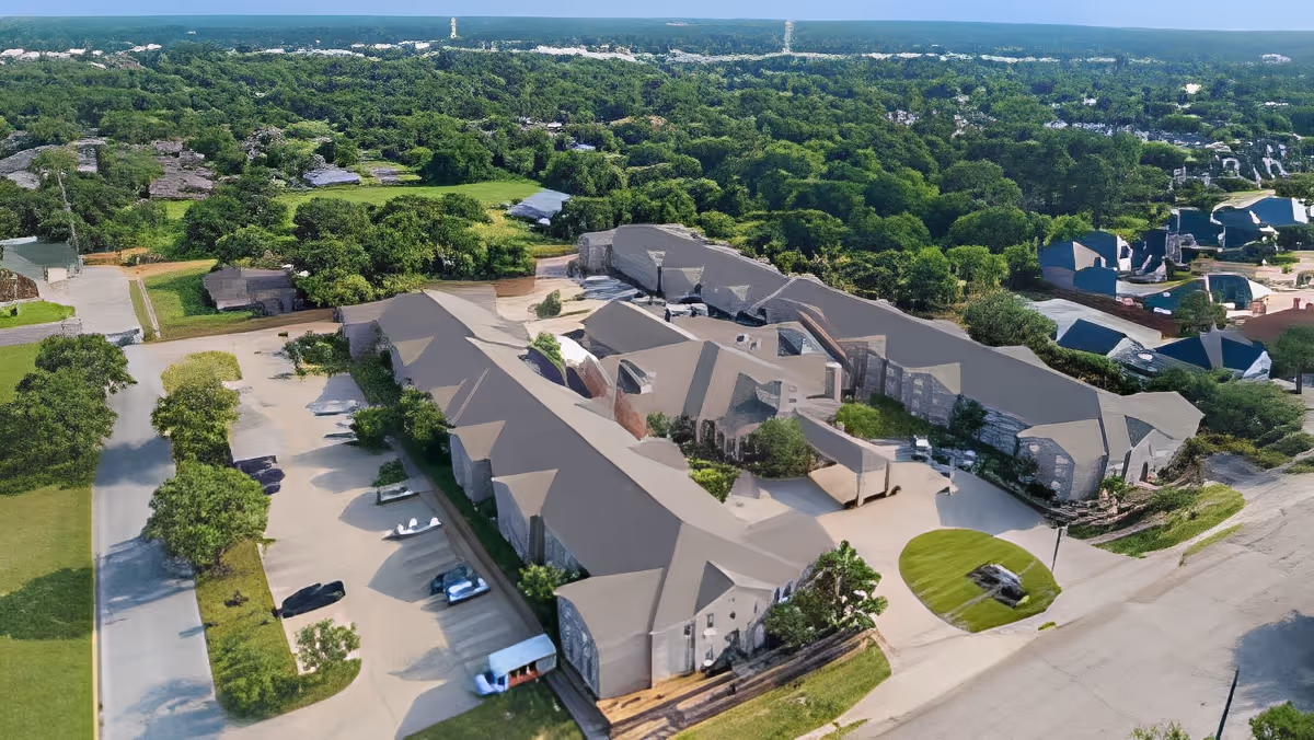 Aerial view of a senior living facility named Morada Pantego surrounded by greenery and trees, with parking areas and roads visible around the building.