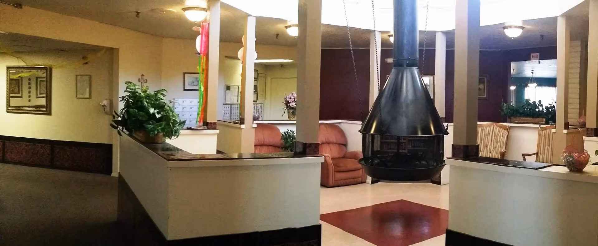 Common area with a suspended black fireplace, couches, and potted plants in a senior living facility.