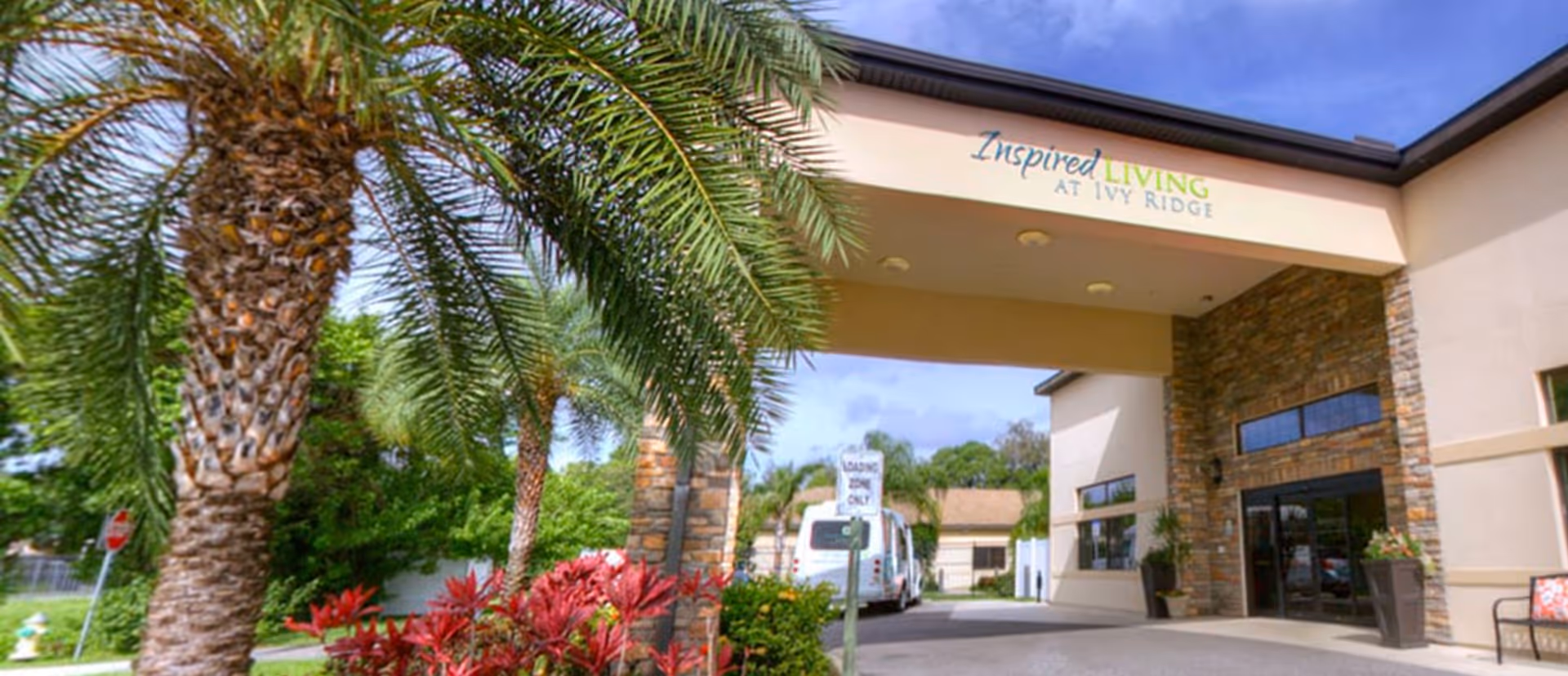Entrance canopy of Inspired Living at Ivy Ridge with palm trees, landscaping and a driveway with a shuttle van.