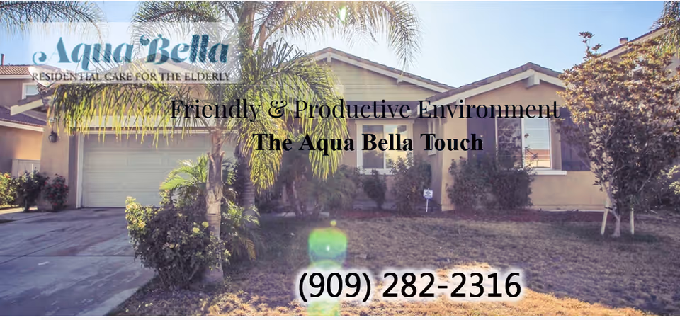 Exterior view of a single-story residential building with a driveway, garage, palm trees, and bushes in the front yard under a clear sky.