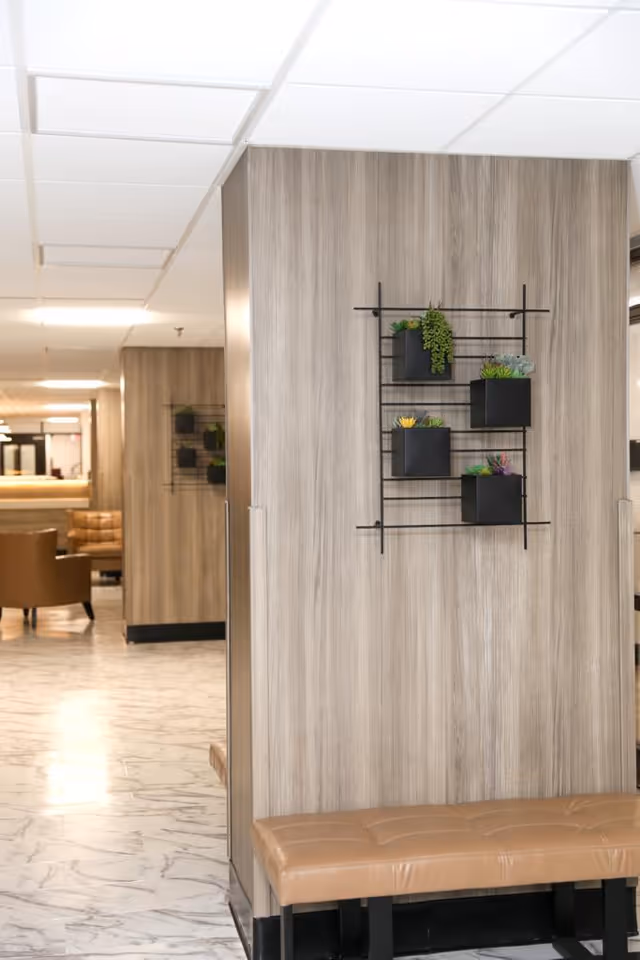 A modern hallway seating area with wood-paneled walls, a leather bench, wall-mounted plant shelves, and marble-look flooring.