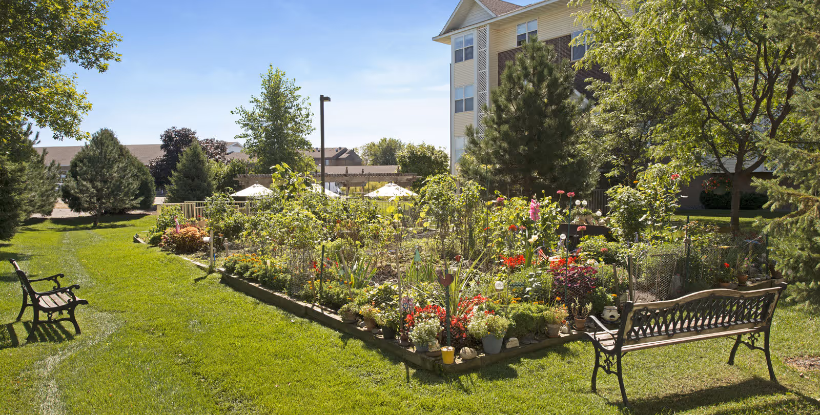 Well-maintained outdoor garden with flower beds, benches, and a multi-story building in the background.