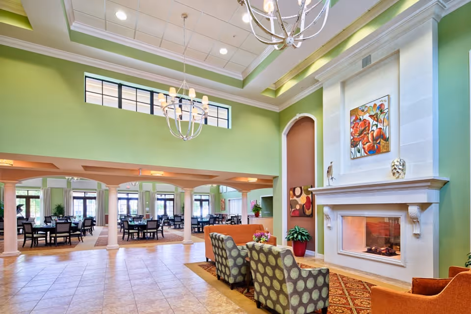 Bright communal dining and lounge area with chandeliers, a fireplace, and multiple tables and chairs.