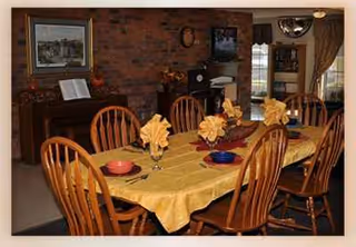 Indoor dining room with a yellow tablecloth, wooden chairs, and brick-wall backdrop.