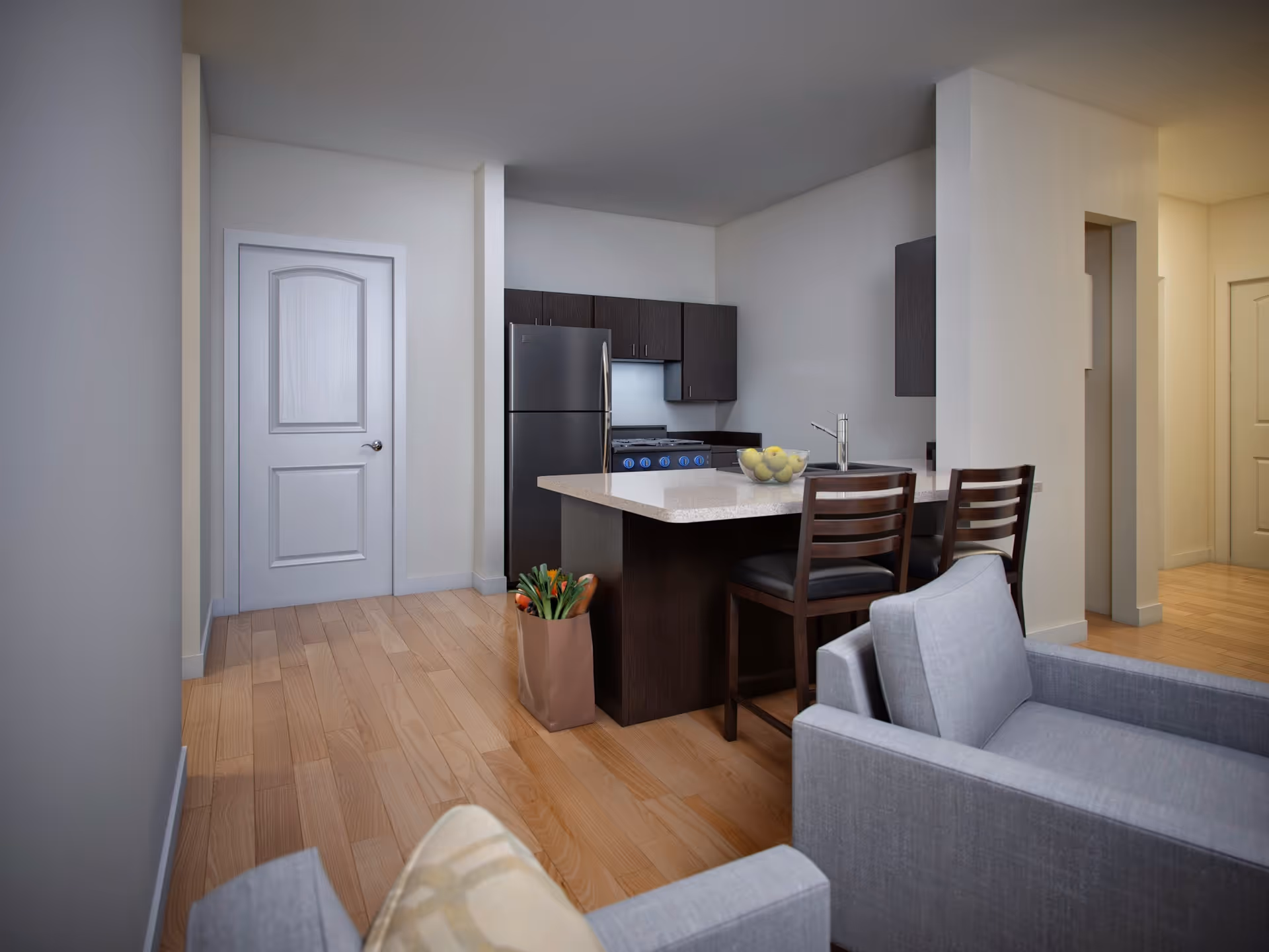 Open-plan interior showing a kitchen island with two bar stools, stainless steel refrigerator and stove, and gray seating in the foreground.