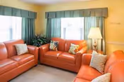 Orange leather sectional sofas form a cozy living room with green curtains and a lamp.