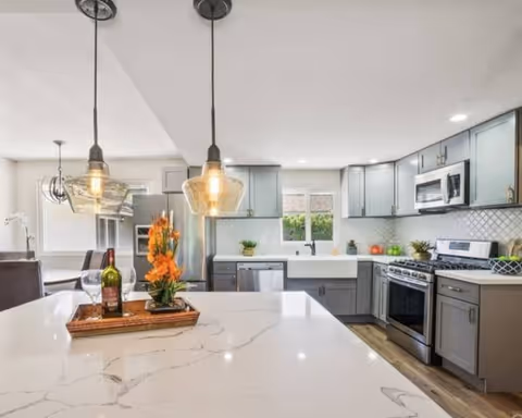 Modern kitchen with island, pendant lights, gray cabinets, and stainless steel appliances.