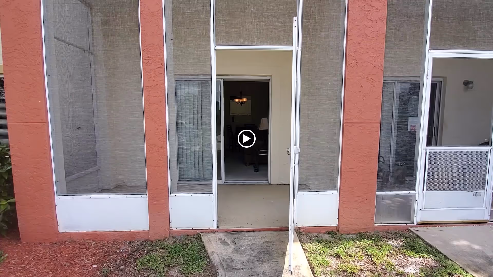 Ground-level screened patio with an open door leading into an interior living area and a short concrete walkway.