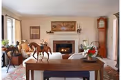 Spacious living room with sofas facing a fireplace, a wooden console table topped with a horse sculpture and flowers, and a tall grandfather clock.