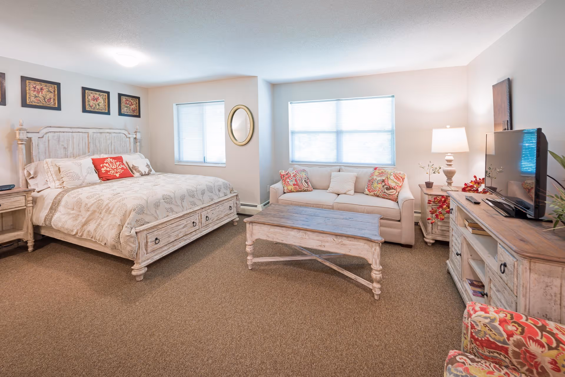 Spacious bedroom suite with a king-size bed, sofa, wooden coffee table and TV in light rustic furnishings.