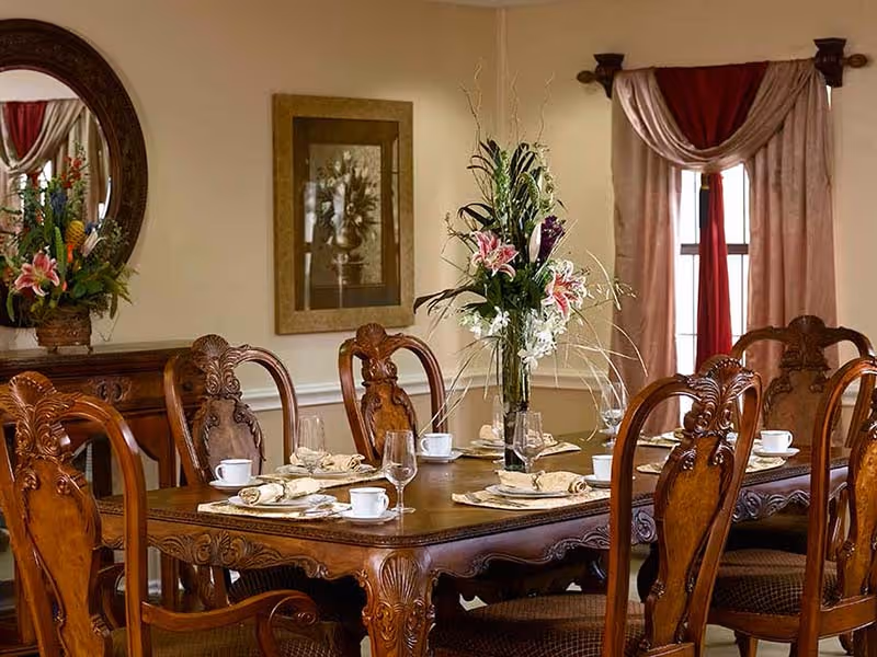 Elegant dining room with an ornate wooden table and chairs set with place settings and a tall floral centerpiece.