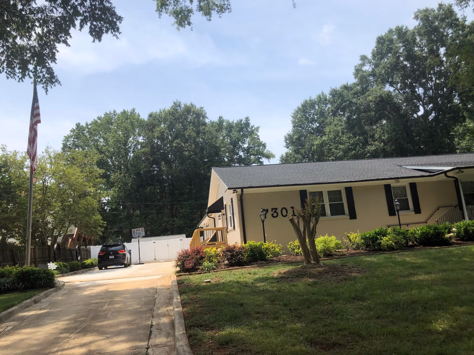 Single-story building with number 301, a driveway with a parked car, flagpole, and surrounding lawn and trees.