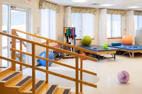 Interior rehabilitation area with a wooden staircase railing, exercise mats, and colorful therapy balls.
