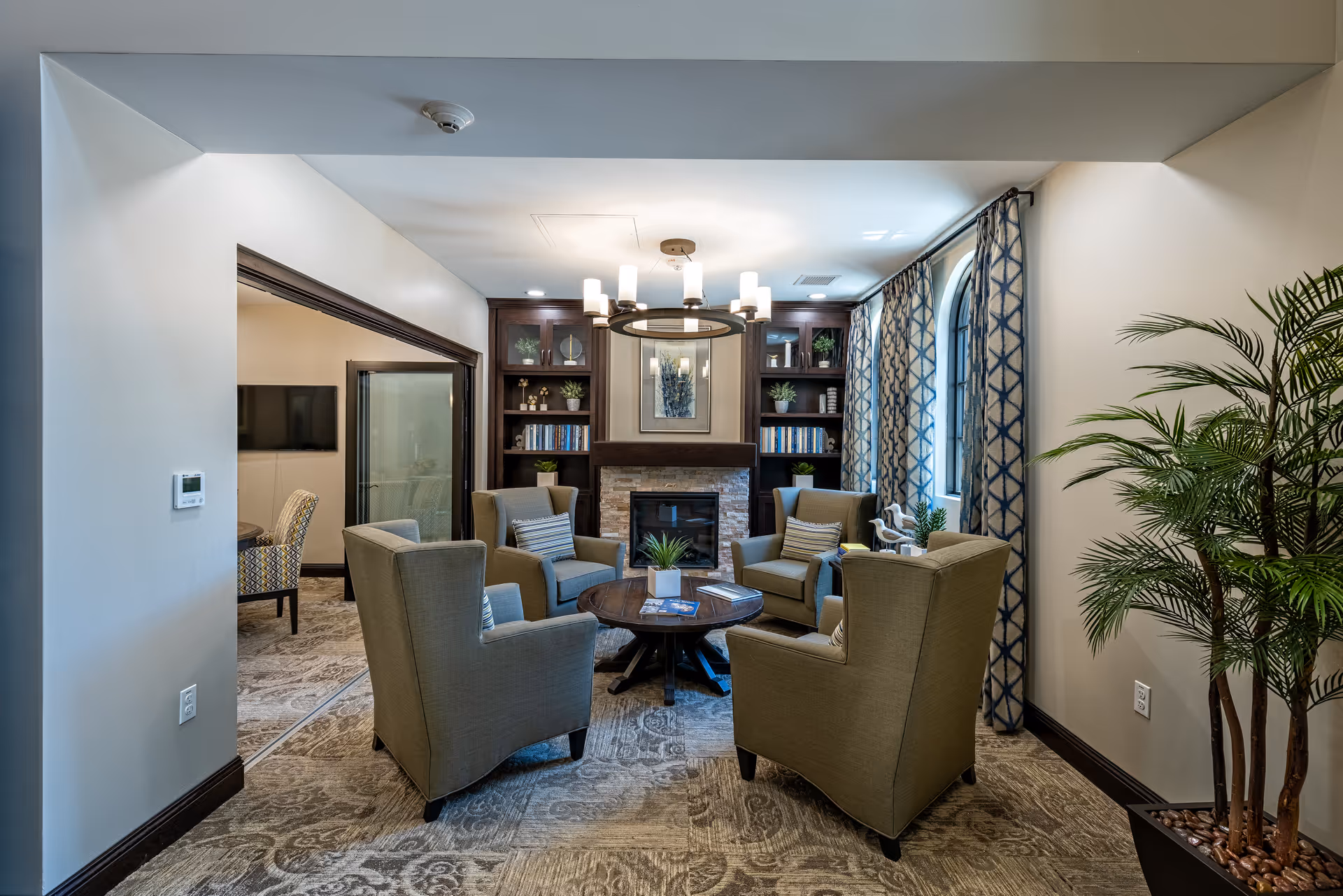 Cozy lounge with armchairs arranged around a central coffee table facing a fireplace and built-in bookshelves.