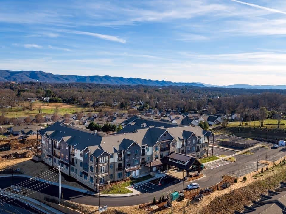 Aerial view of a large multi-story senior living facility named Everlan of Johnson City, surrounded by a parking lot and residential neighborhood with mountains in the background under a partly cloudy sky.