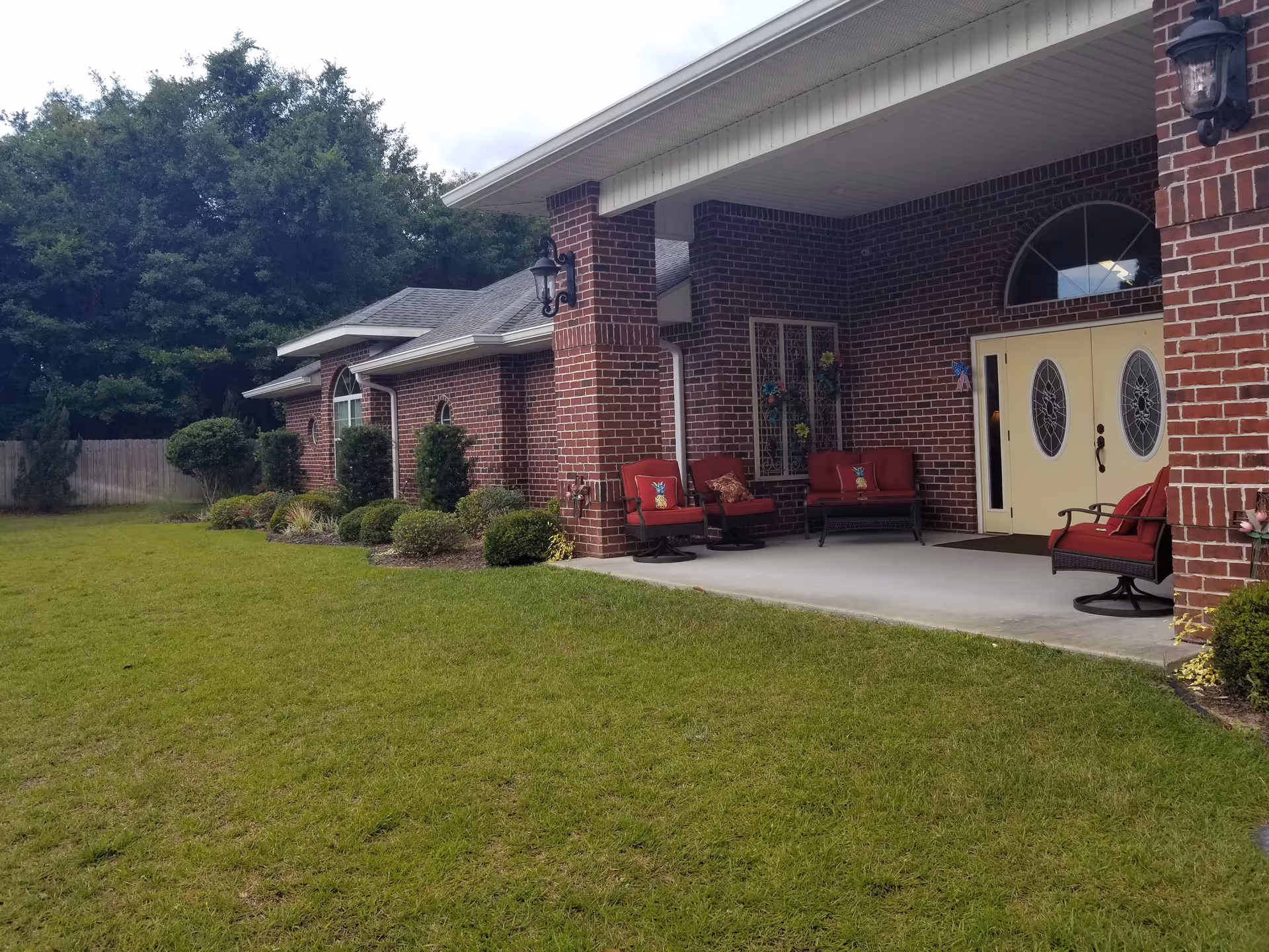 Brick building front with a covered porch, red patio chairs, double decorative doors and a grassy lawn.