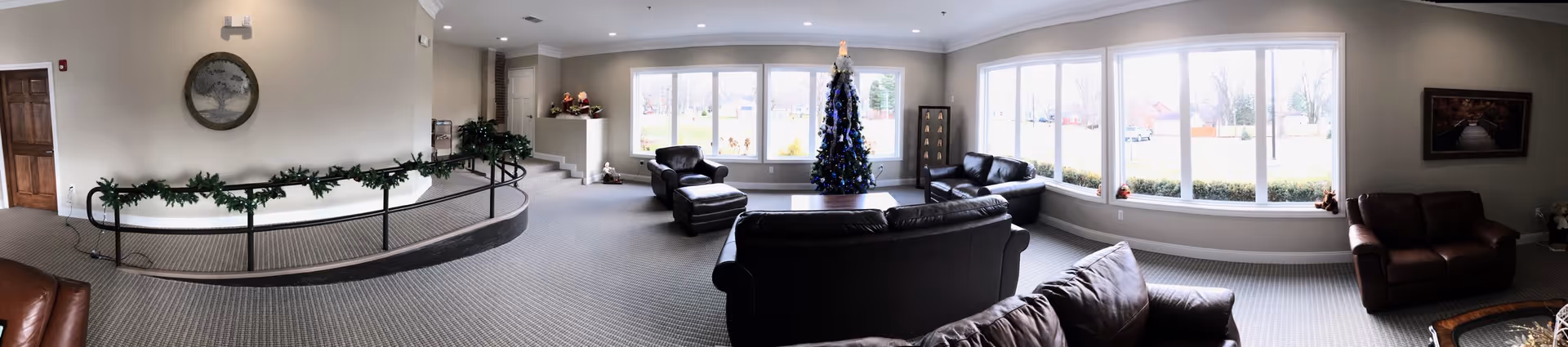 Spacious senior living common room with leather sofas, a decorated Christmas tree, and large windows overlooking the grounds.