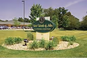 Entrance sign for West Woods of Niles Nursing Center on a landscaped lawn with the building and parked cars in the background.