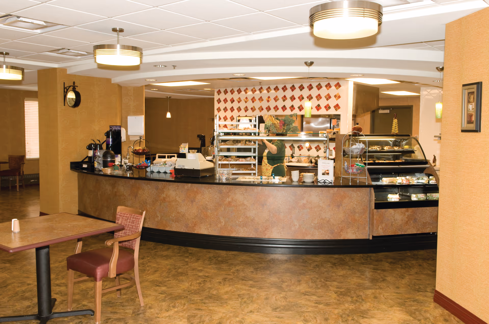 A dining/cafeteria area with a curved service counter, food display cases, and seating.